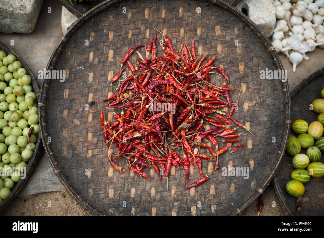 Red Dried Chilis On Bamboo Platter Myinkaba Myanmar // MYINKABA, Myanmar — Red dried chilis are displayed on a woven bamboo platter at the morning market in Myinkaba village. The village is located near Bagan in Myanmar's Mandalay Region, an area known for its agricultural production. Local vendors typically sell fresh produce, spices, and traditional foods at these community markets. Myinkaba serves as one of several villages surrounding the ancient temple complex of Bagan. The morning markets are an important part of daily commerce in rural Myanmar communities. Traditional woven bamboo platt Stock Photo