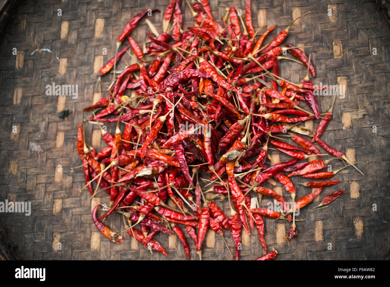 Red Dried Chilies Myinkaba Myanmar // MYINKABA, Myanmar — Red dried chilis are displayed on a woven bamboo platter at the morning market in Myinkaba village. The village is located near Bagan in Myanmar's Mandalay Region, an area known for its agricultural production. Local vendors typically sell fresh produce, spices, and traditional foods at these community markets. Myinkaba serves as one of several villages surrounding the ancient temple complex of Bagan. The morning markets are an important part of daily commerce in rural Myanmar communities. Traditional woven bamboo platters and baskets a Stock Photo