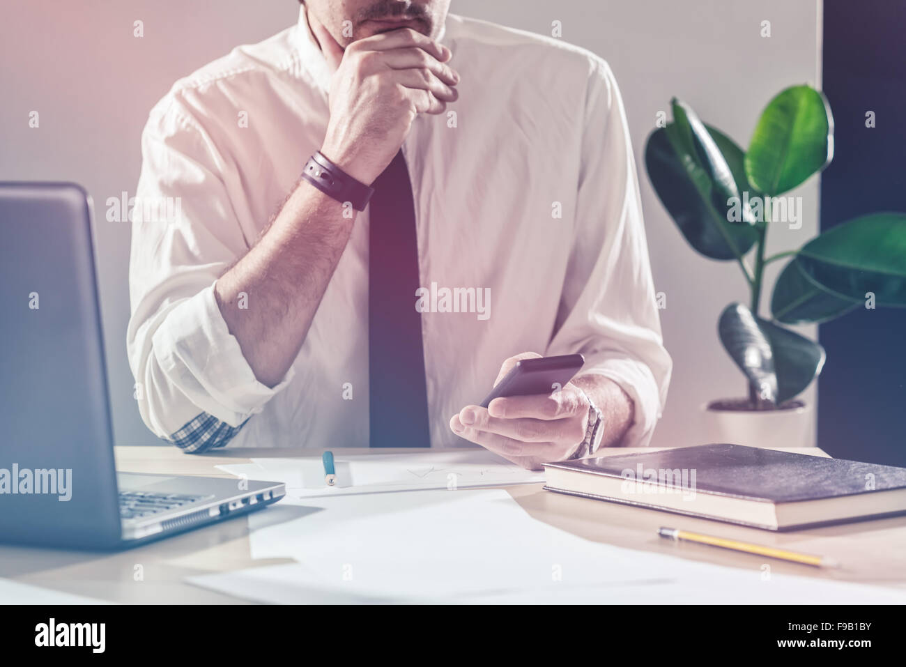 Businessman using mobile phone, working overtime at office desk