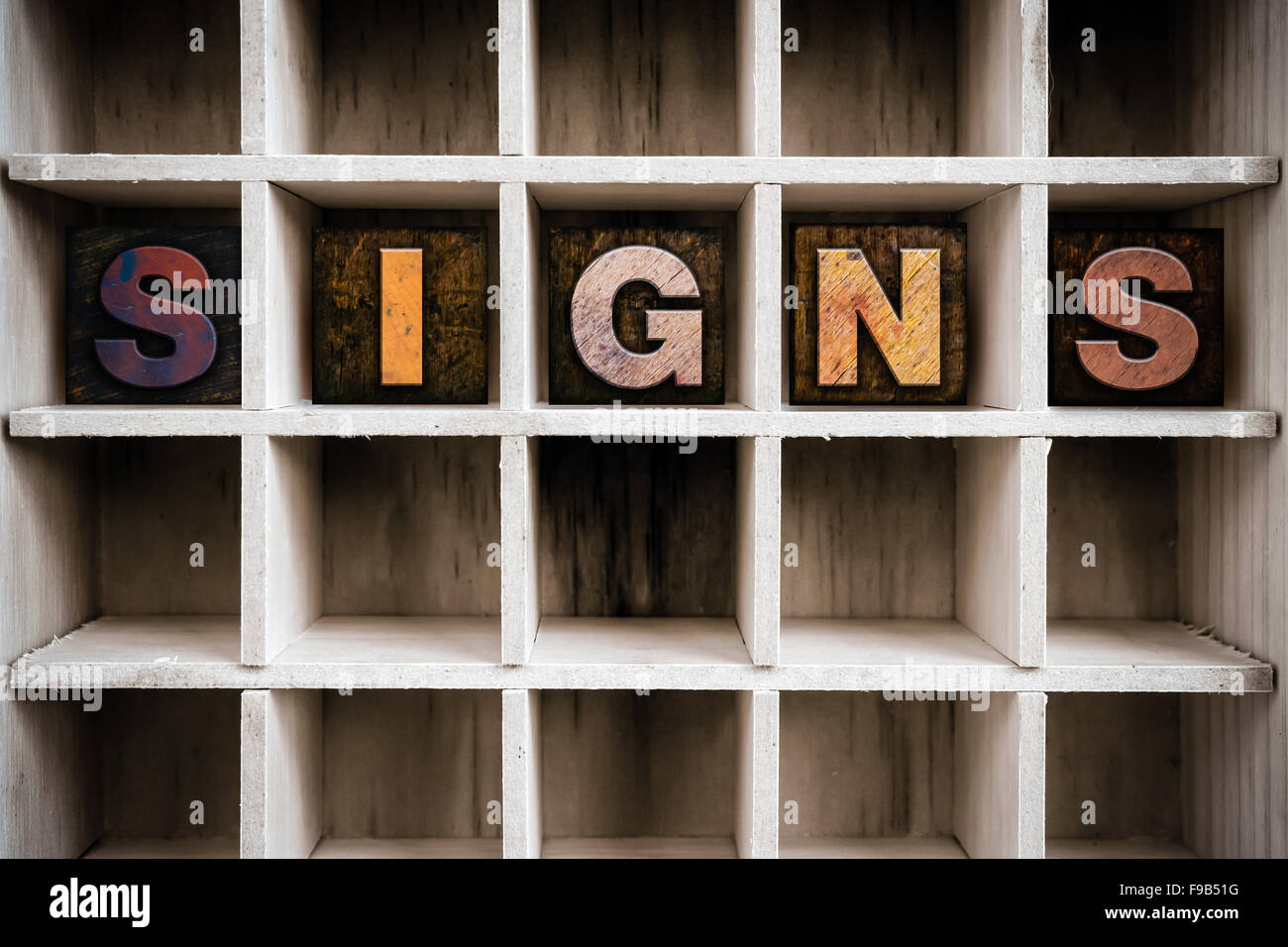 The word "SIGNS" written in vintage ink stained wooden letterpress type in a partitioned printer's drawer. Stock Photo