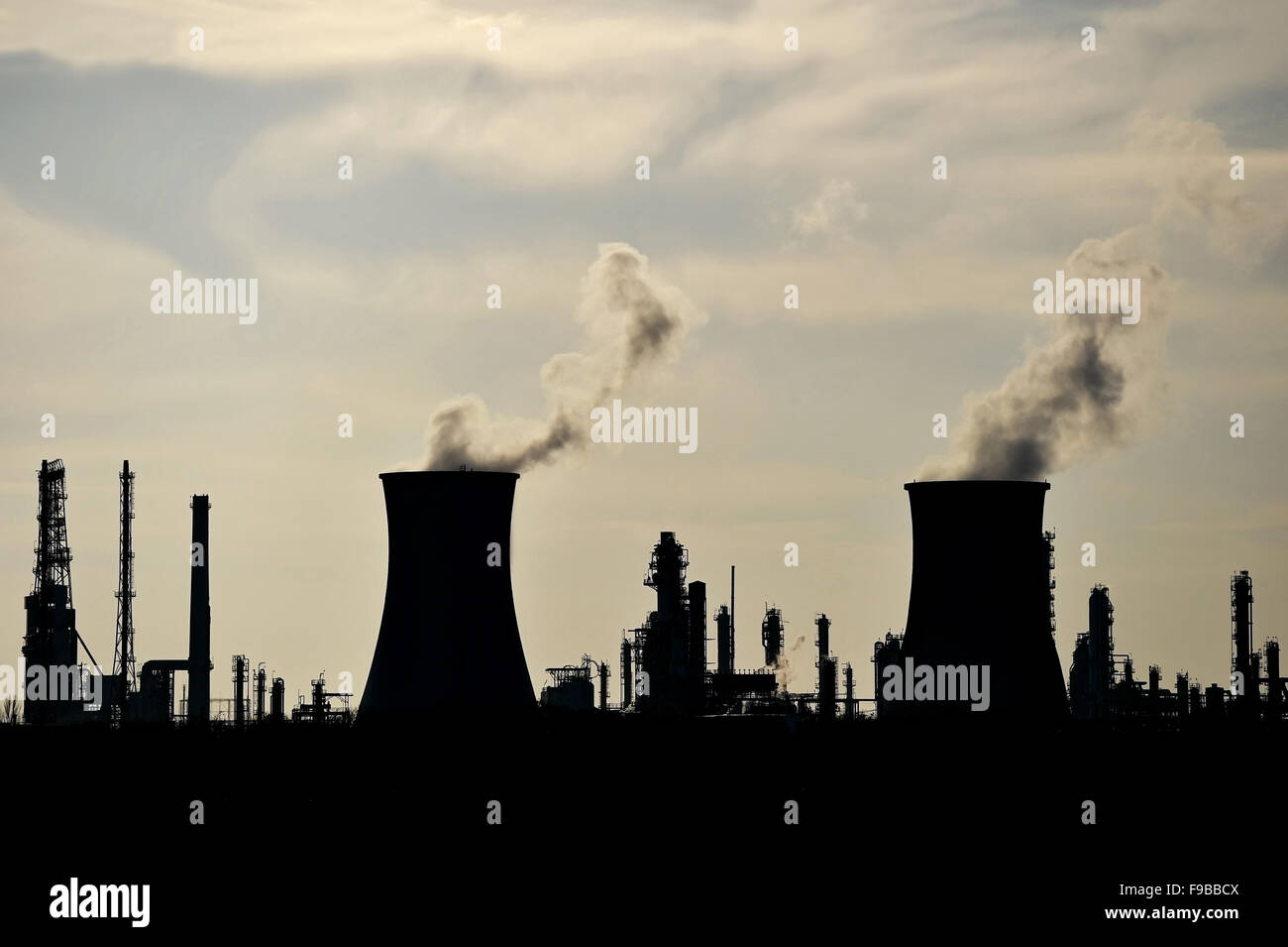 Smoke and steam coming out from industrial petrochemical plant chimneys silhouetted against the sky Stock Photo