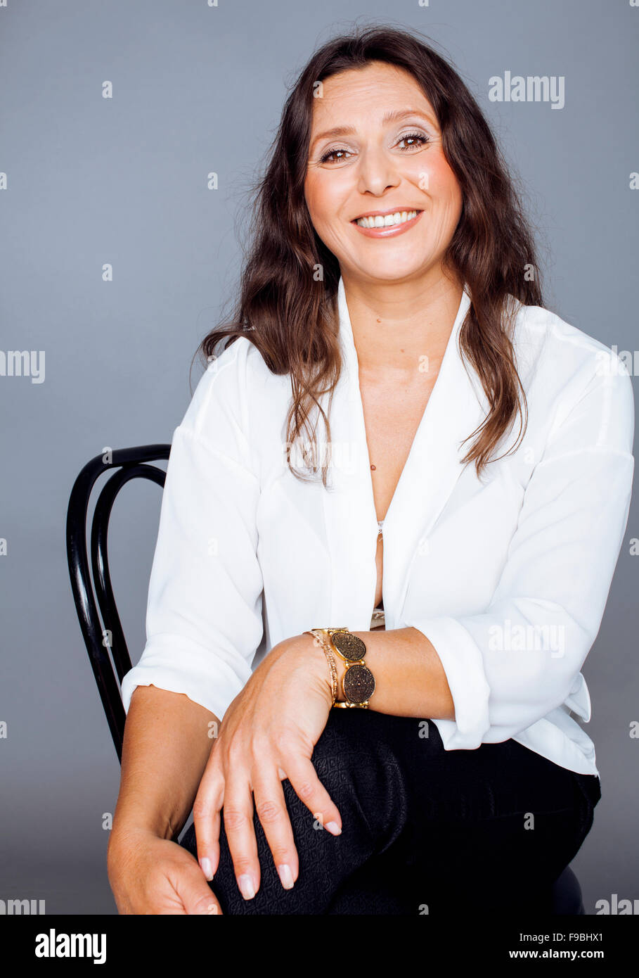 pretty brunette confident mature woman sitting on chair in studio smiling  tender Stock Photo - Alamy