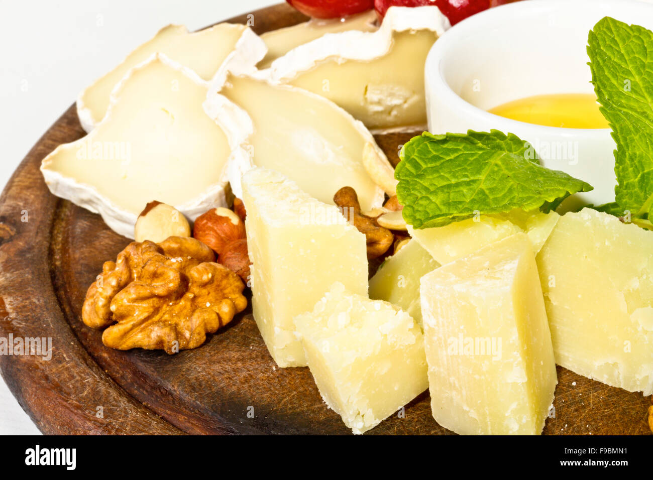 Various types of cheese with honey, nuts and grapes on plate, isolated