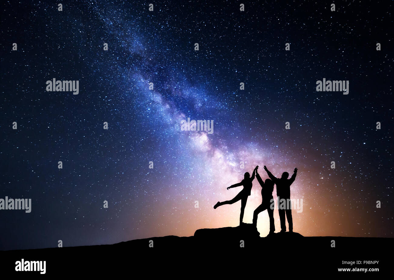 Milky Way. Night sky with stars and silhouette of a happy family with raised-up arms Stock Photo