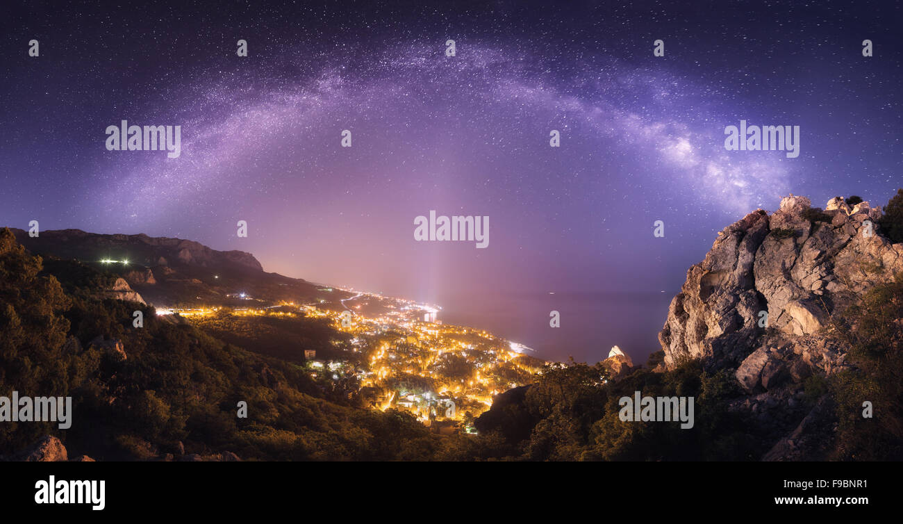 Beautiful night landscape with Milky Way against city lights, mountains, sea and starry sky. Nature background Stock Photo