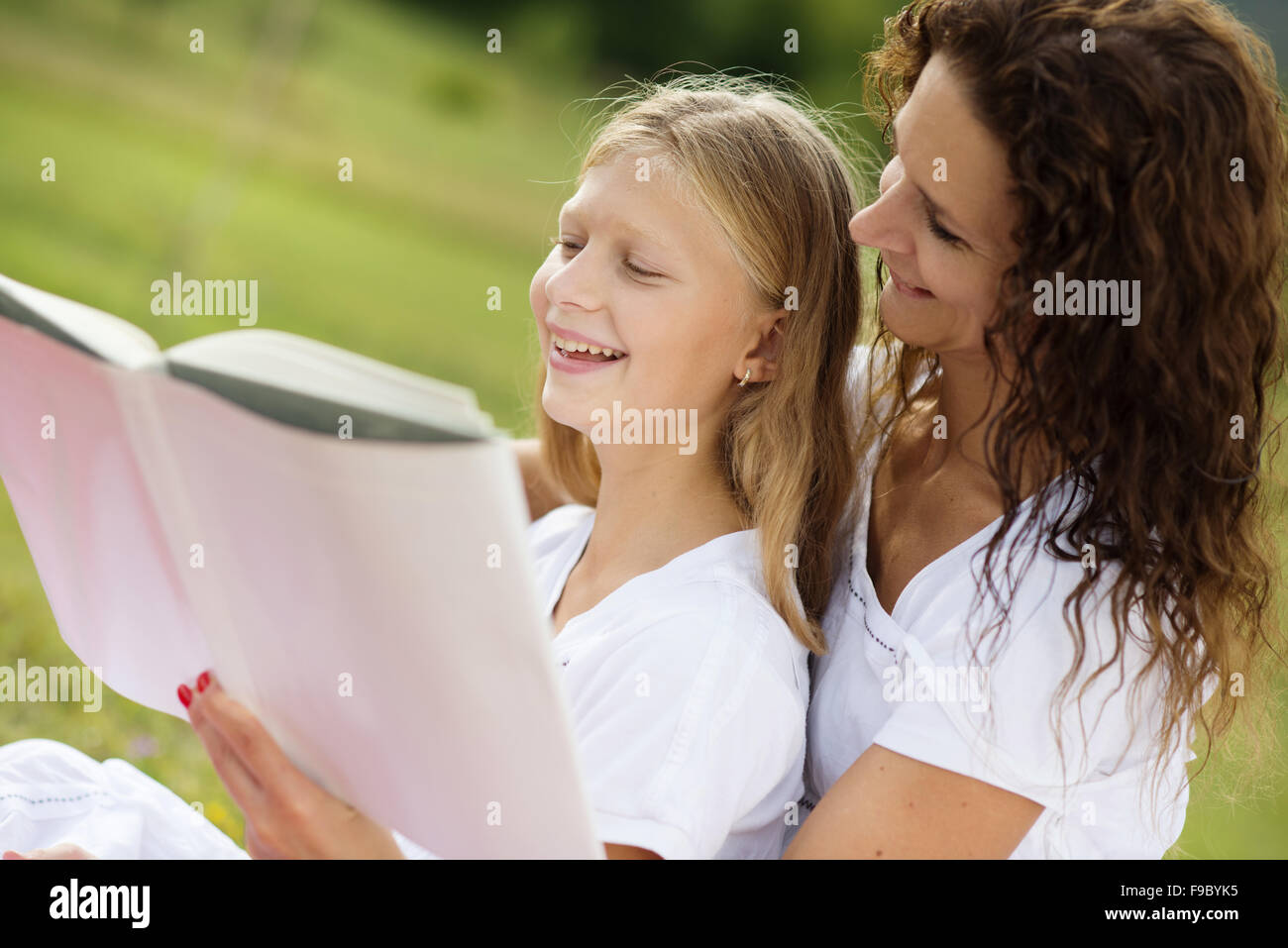 Mother is seating and reading a book to her children in the green park Stock Photo