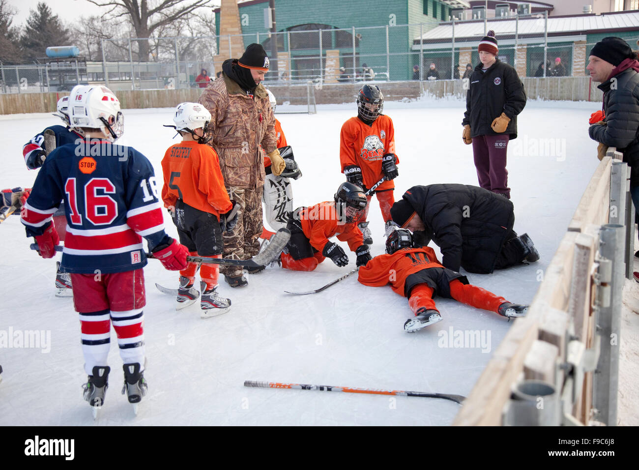 Coach attending to a downed boy age 10 with a sports injury during an outdoor hockey game. Phalen Park. St Paul Minnesota MN USA Stock Photo