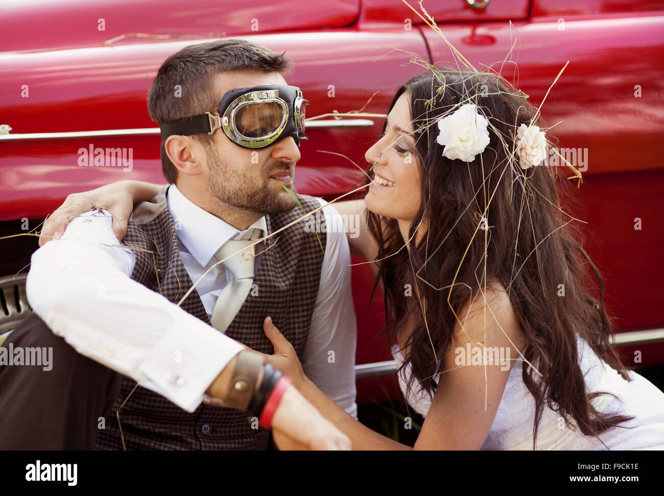 Gorgeous bride and groom having fun with red retro car in nature Stock