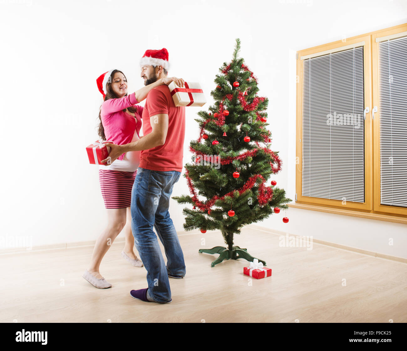 Young couple is dancing close to christmas tree. Woman is pregnant. Stock Photo