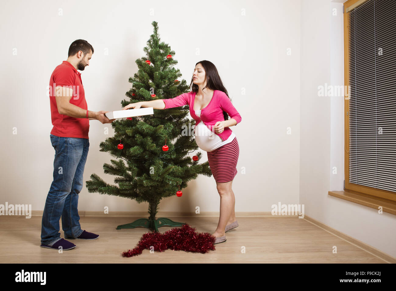 Young couple is decorating christmas tree. Woman is pregnant. Stock Photo