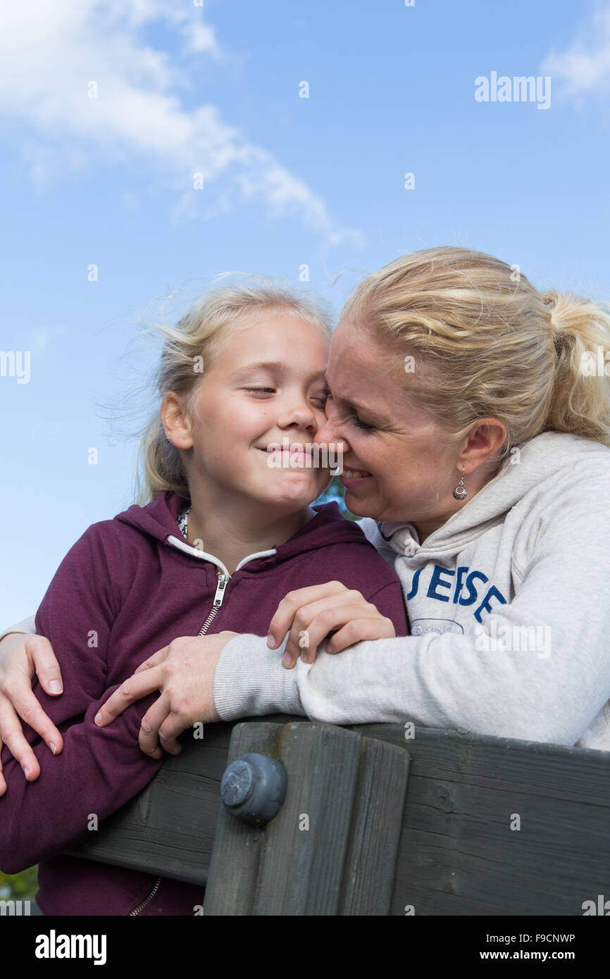 A mother and a daughter hugging and nuzzling against a blue sky Stock