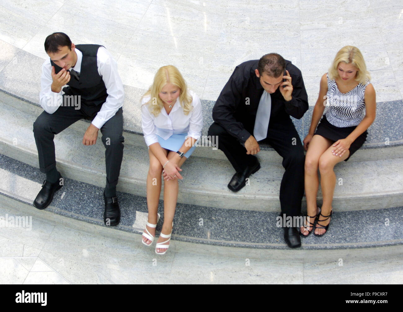 Four Young People Sitting on Stairs in Huge Hall Stock Photo