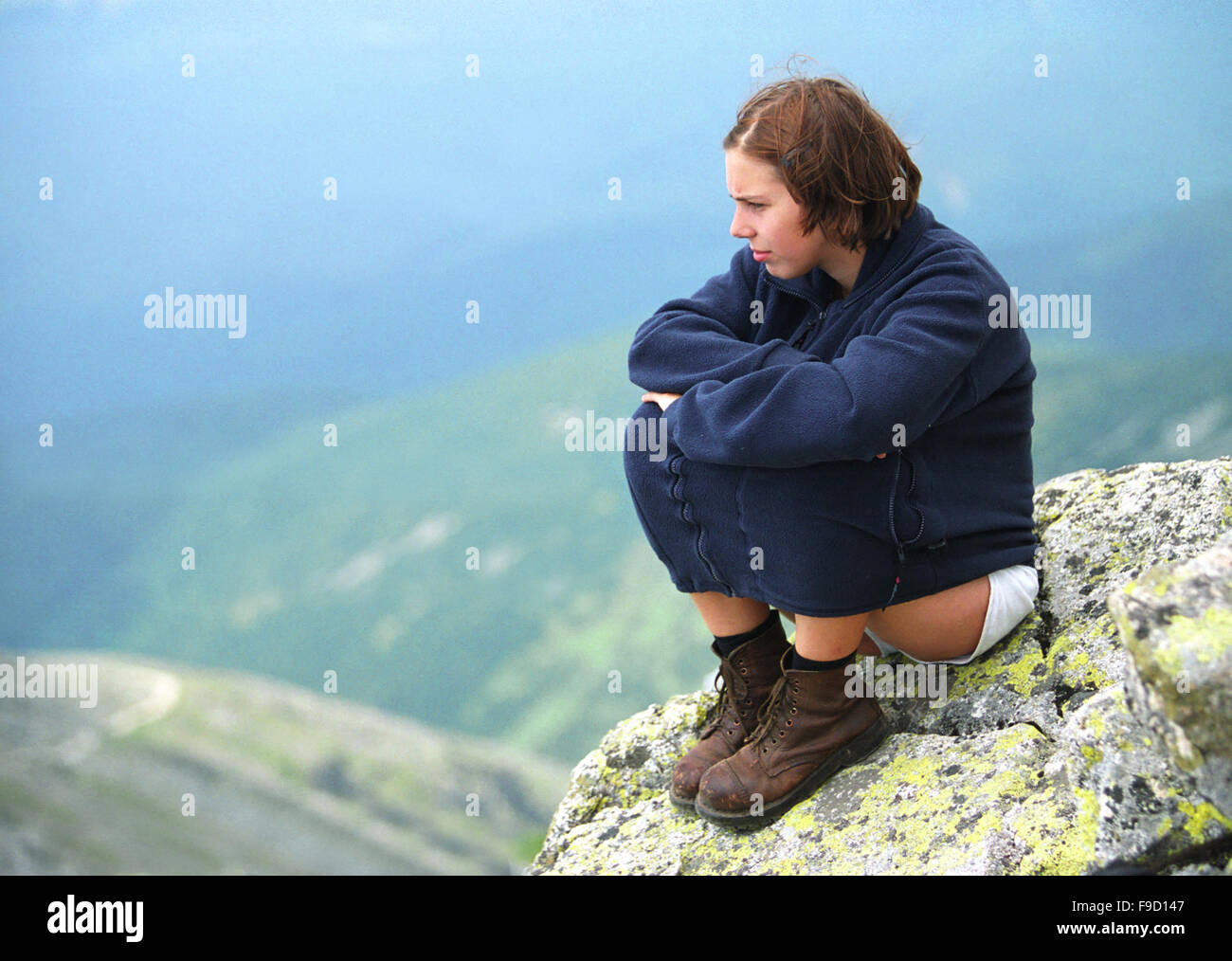 Sad Girl Sitting on The Rocky Top Stock Photo