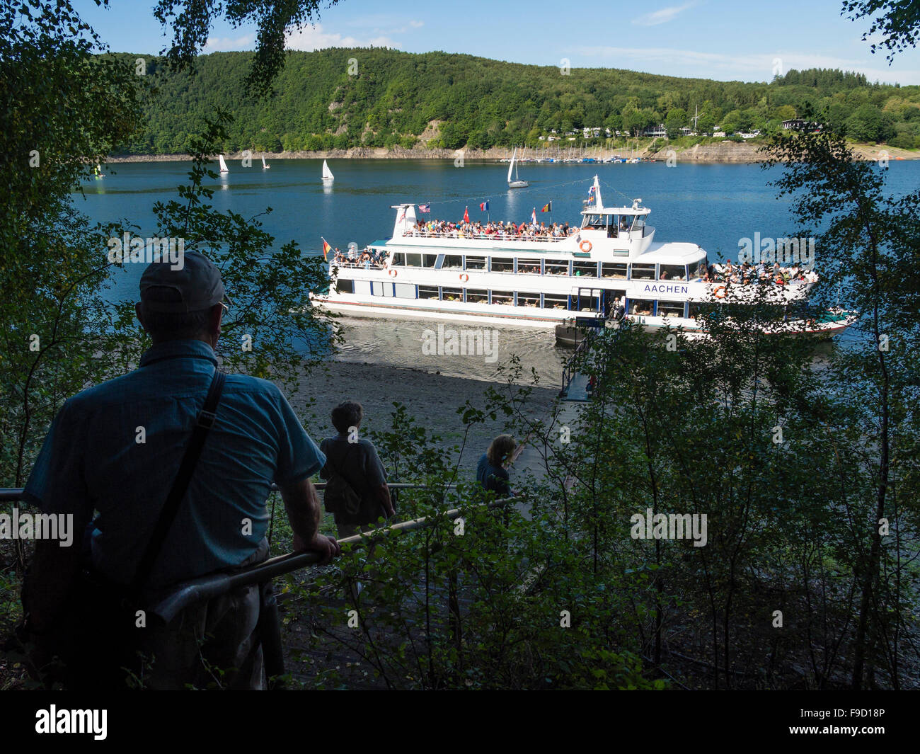 Tourists on the banks of the Rursee lake wait for the arrival of a passenger ship in the German Eifel National Park. Stock Photo