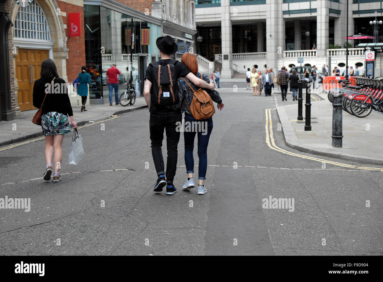 Rear view of a young hipster couple walking towards Liverpool St. along Brushfield Street near Spitalfield Market in London UK  KATHY DEWITT Stock Photo