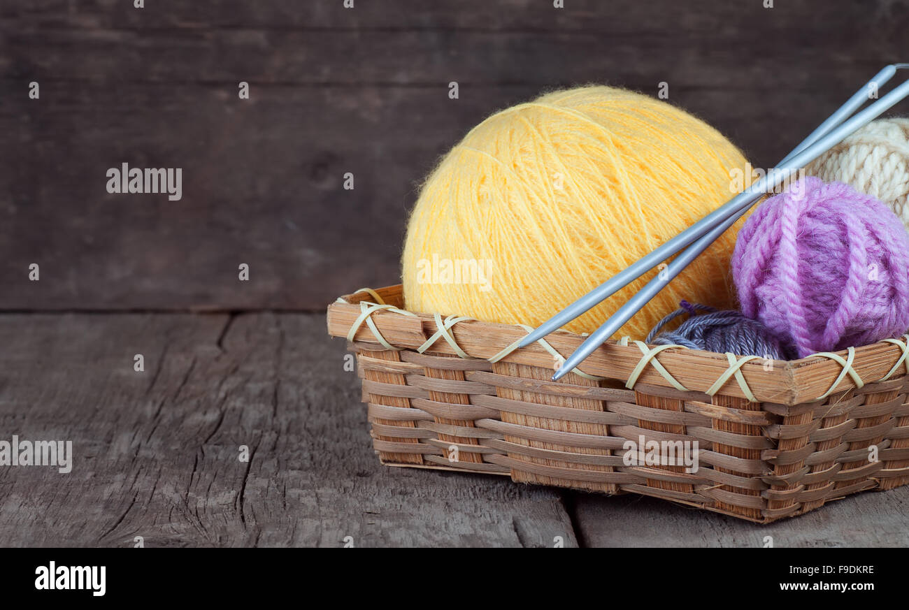 Balls of yarn in basket with knitting needles on wooden background Stock Photo