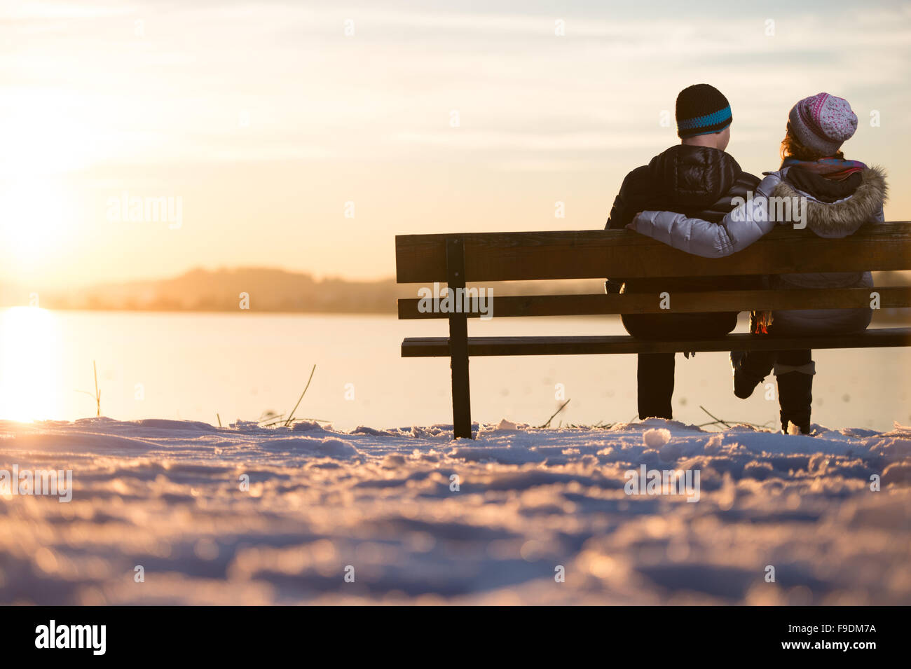 Young couple sitting on a bench in the sunset in front of a lake Stock ...