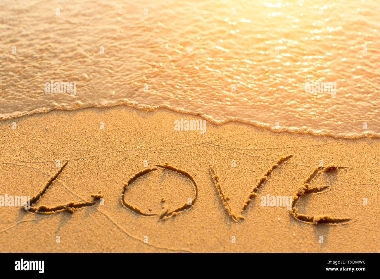 Inscription LOVE on sea beach sand, is soft the wave. Stock Photo