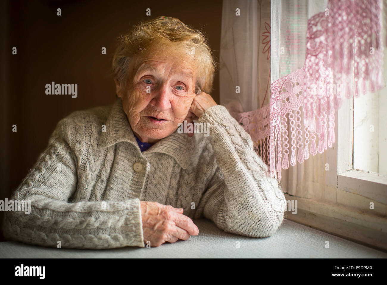 An elderly woman sits alone near the window. Stock Photo