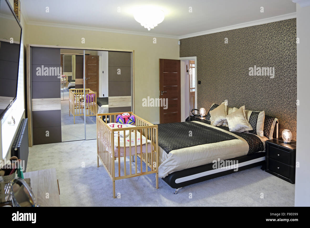 A newly decorated modern bedroom with a double bed and a baby's cot contrasting with the trendy furniture Stock Photo