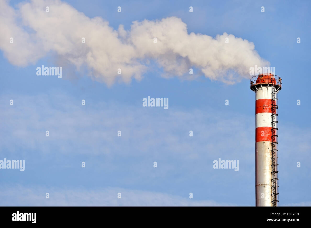 Smoke and steam coming out from an industrial petrochemical plant chimney with a blue sky on the background Stock Photo
