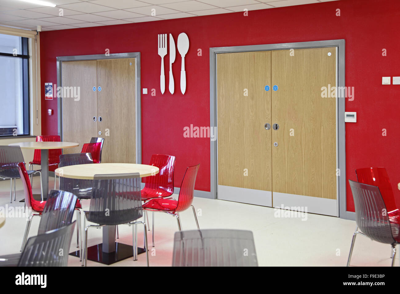 restaurant area in a new academy school featuring a red and grey colour scheme with large knife and fork symbols mounted on wall Stock Photo