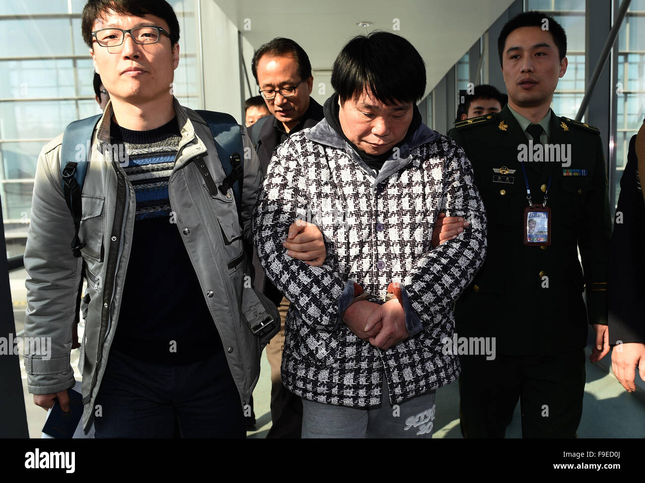 Nanjing, Jiangsu, China. 16th December, 2015. Fugitive Kang Taeyong (C, front) is escorted at Lukou international airport in Nanjing. Chinese police on Wednesday handed over a Korean fugitive on Interpol's Most Wanted List to their Republic of Korea (ROK) counterparts at Nanjing airport. It is alleged Kang Taeyong, 54, extorted about 1.5 trillion won (about 1.2 billion U.S. dollars) from more than 30,000 people in ROK between 2007 and 2008. Interpol listed him as a most wanted fugitive in November 2008, but they suspect he quickly fled to China. Credit:  Xinhua/Alamy Live News Stock Photo