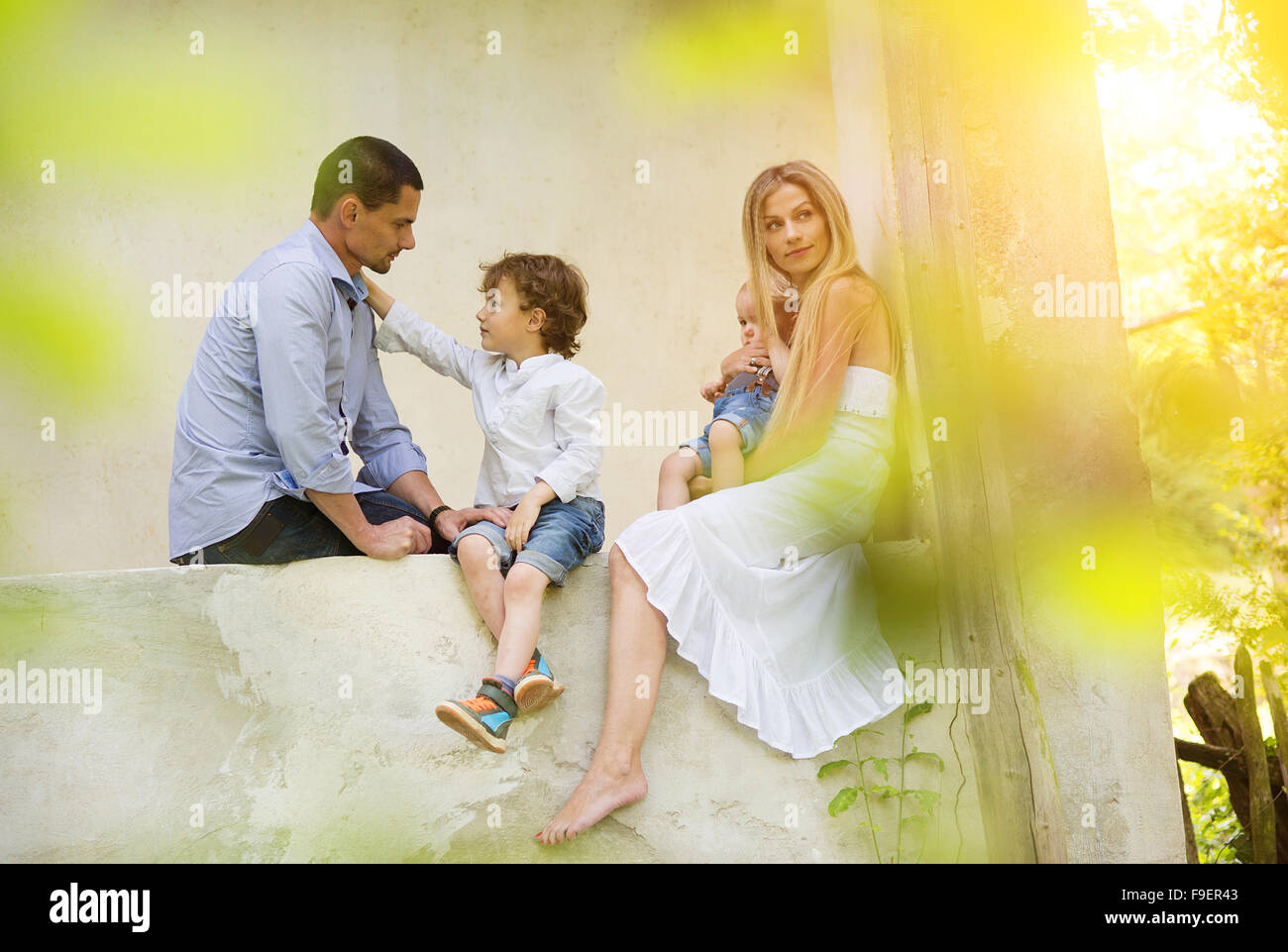 Happy young family spending time together sitting outside on a porch of old house. Stock Photo