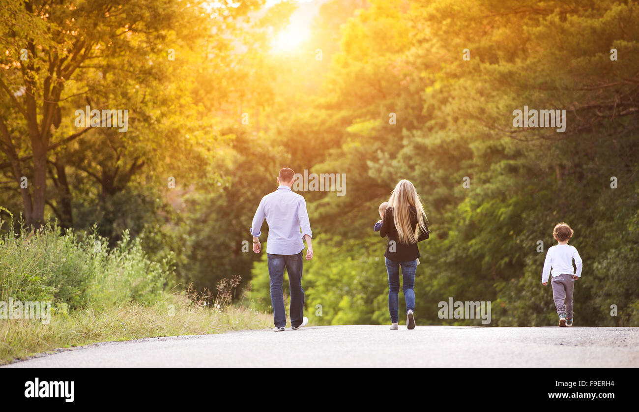 Happy young family walking down the road outside in green nature. Stock Photo