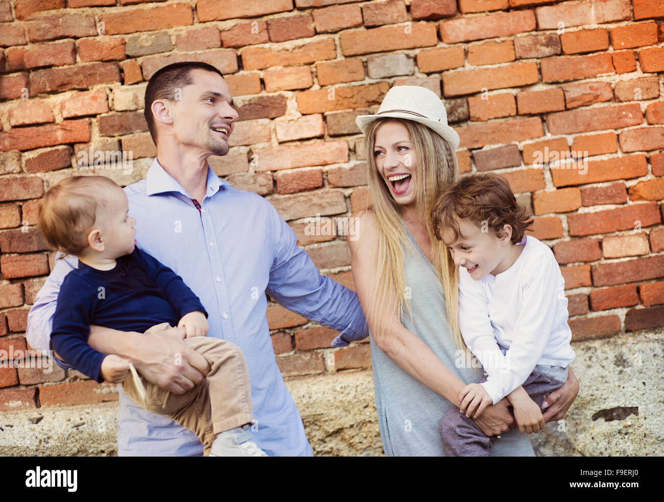 Happy young family spending time together outside by the brick wall. Stock Photo