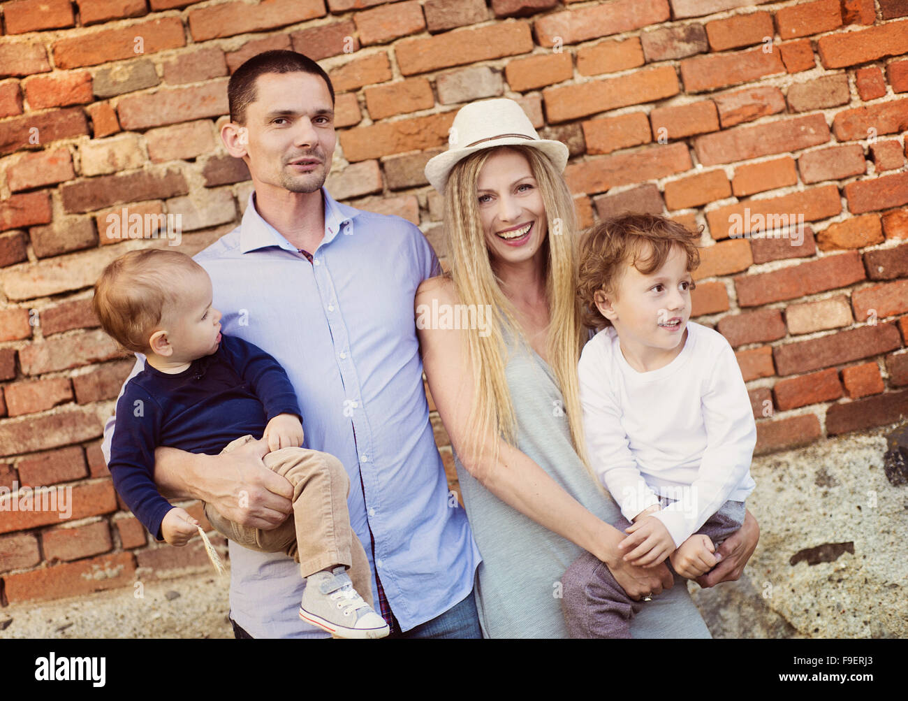 Happy young family spending time together outside by the brick wall. Stock Photo