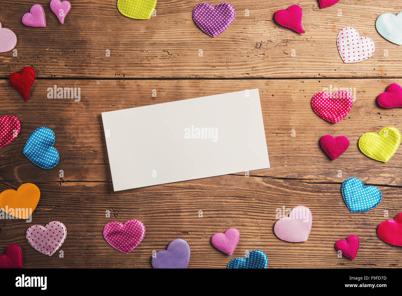 Empty paper sheet and colorful fabric hearts. Studio shot on wooden background. Stock Photo