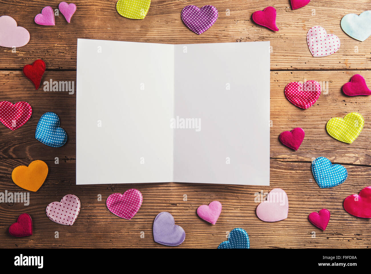 Empty paper sheet and colorful fabric hearts. Studio shot on wooden background. Stock Photo