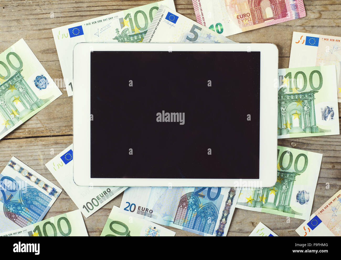 Tablet and European currency banknotes scattered on the wooden table background. View from above. Stock Photo
