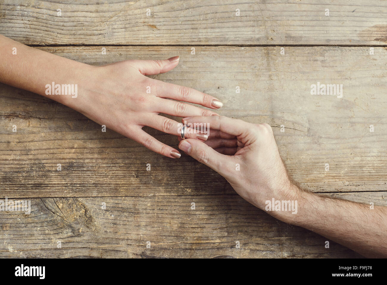 Man putting on engagement ring tenderly to his woman. Studio shot on a wooden background, view from above. Stock Photo