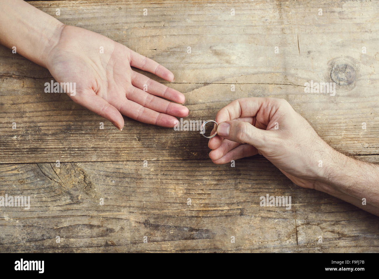 Man offering a wedding ring tenderly to a woman. Studio shot on a wooden background, view from above. Stock Photo