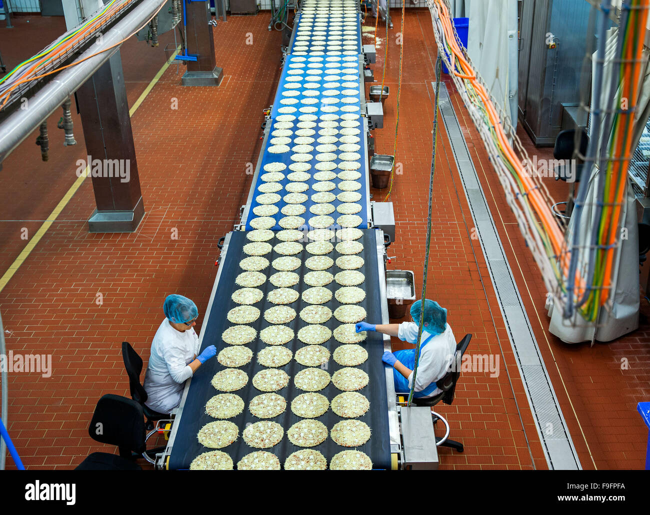 Staff check the production line that is topping frozen pizzas at the