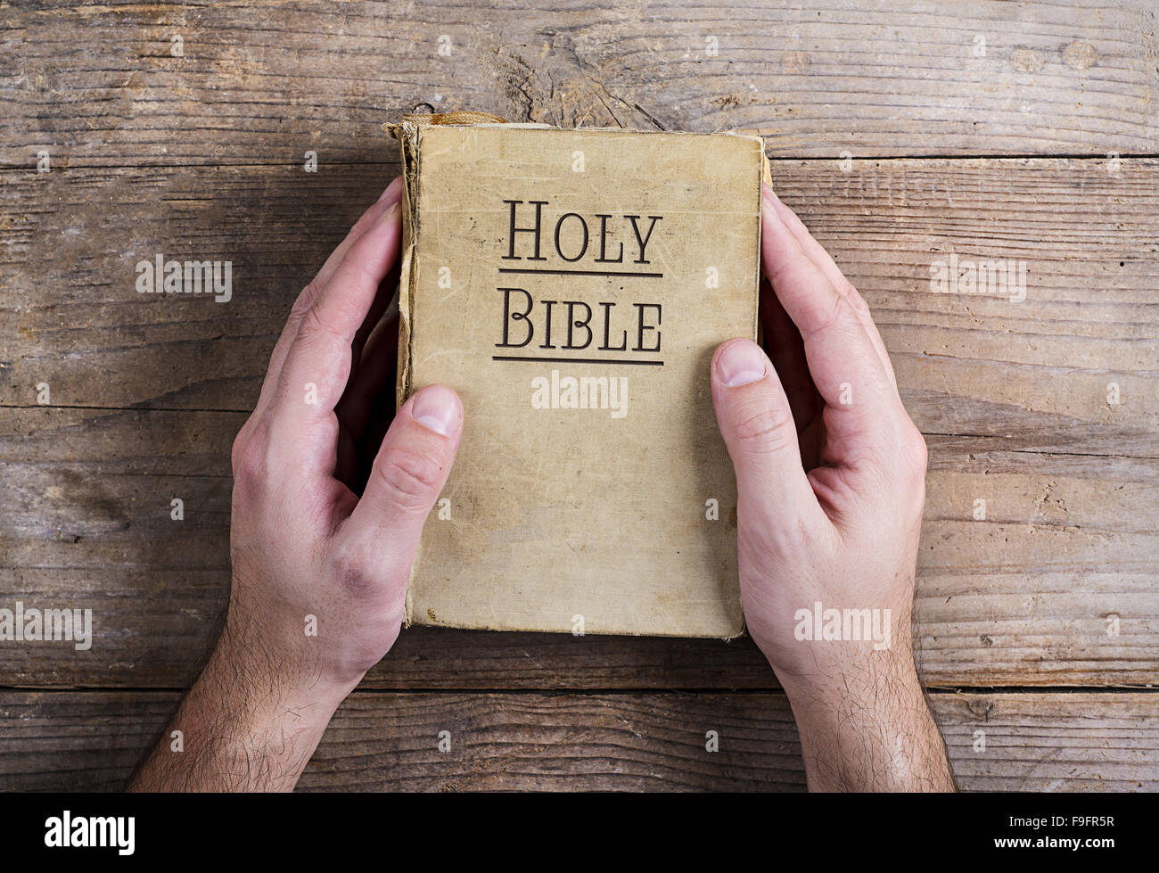 Hands holding Bible on a wooden desk background. Stock Photo