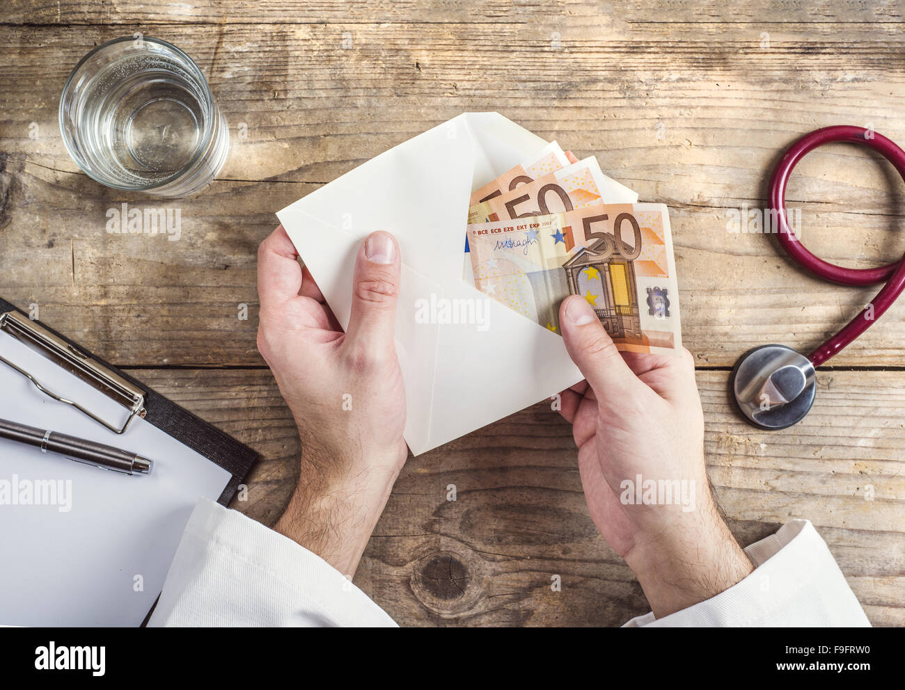 Hands of unrecognizable doctor accepting a bribe. Wooden desk background. Stock Photo