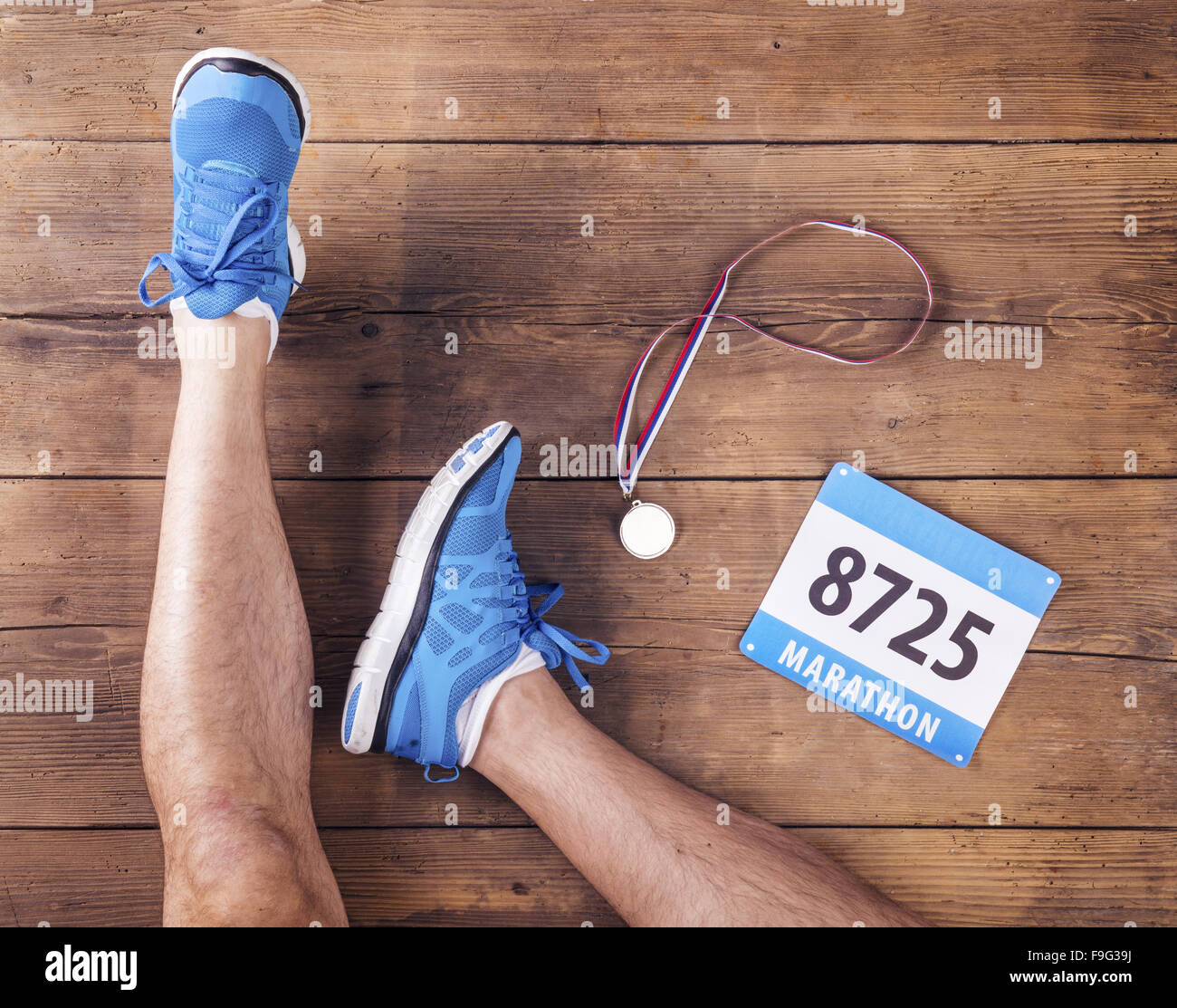 Legs of a runner, medal and race number on a wooden floor background Stock Photo