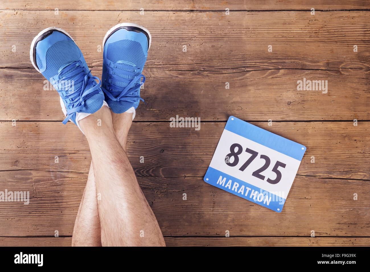 Legs of a runner and race number on a wooden floor background Stock Photo