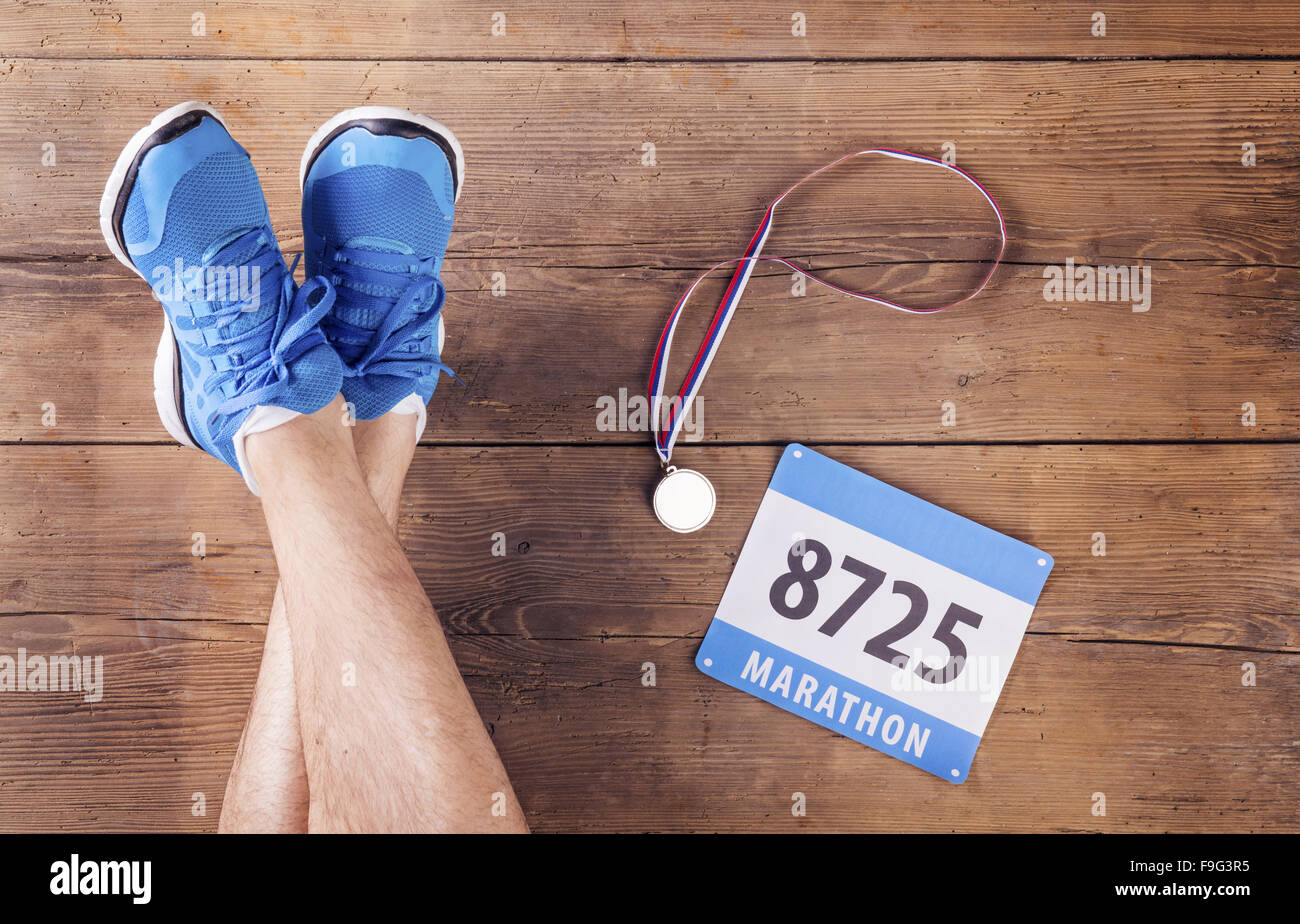 Legs of a runner, medal and race number on a wooden floor background Stock Photo