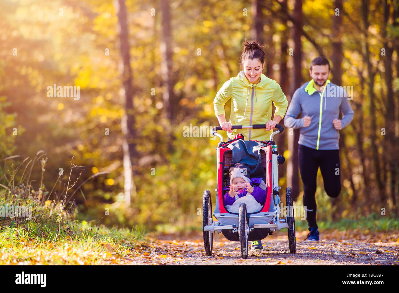Beautiful young family with baby in jogging stroller running outside in autumn nature Stock Photo