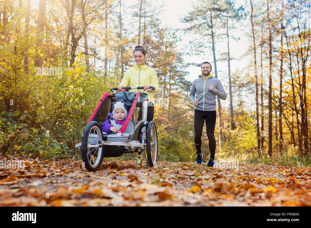 Beautiful young family with baby in jogging stroller running outside in autumn nature Stock Photo