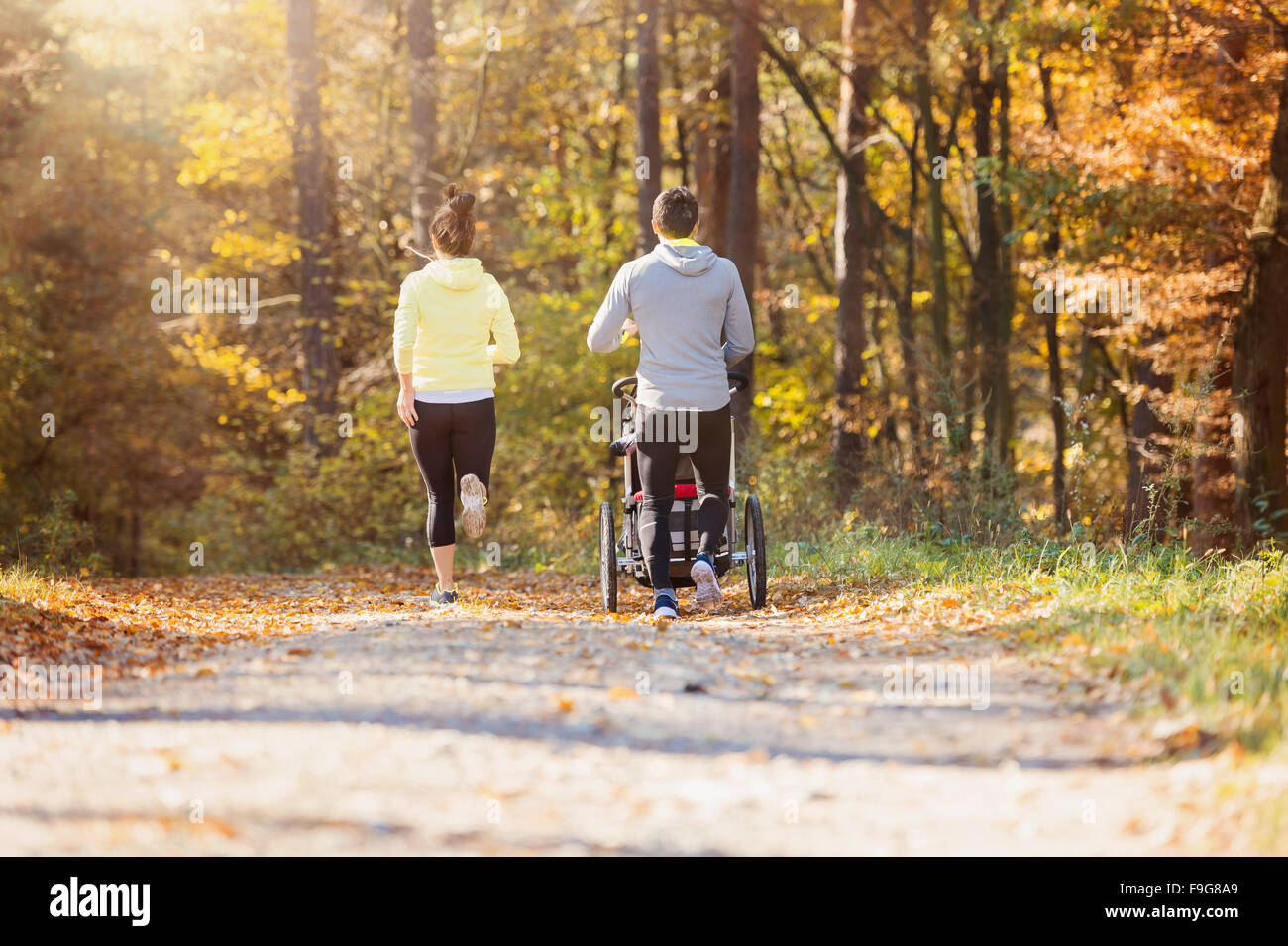 Beautiful young family with baby in jogging stroller running outside in autumn nature Stock Photo