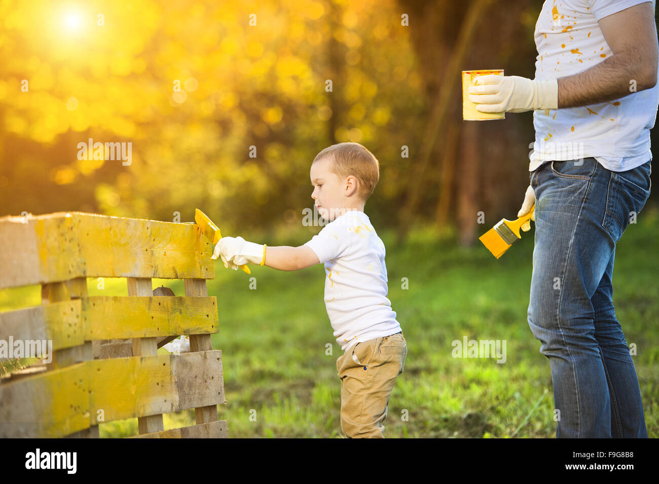 Cute little boy and his father painting wooden fence together on sunny day in nature Stock Photo