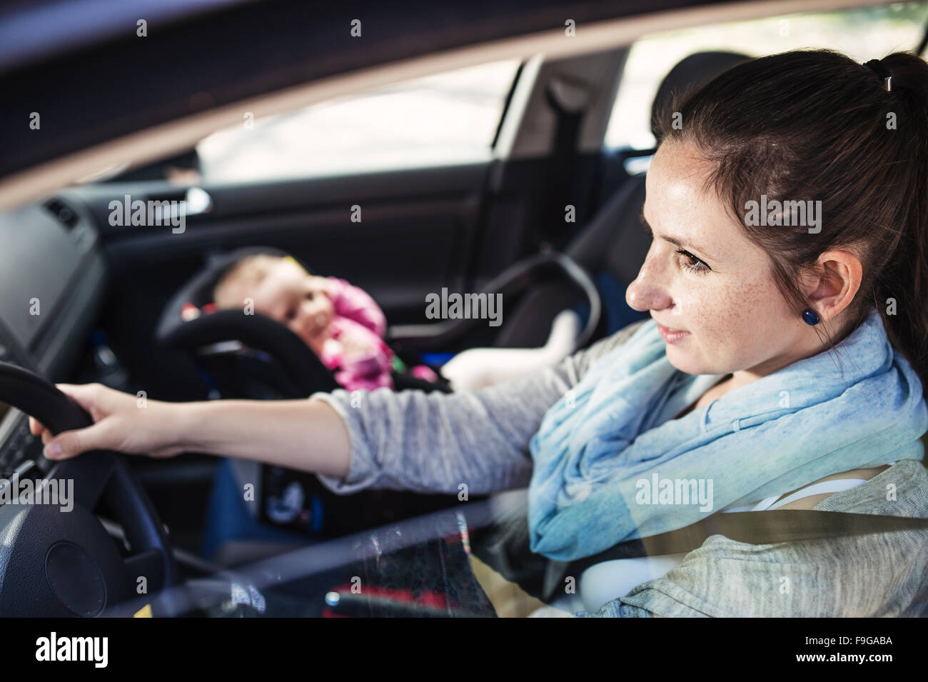 Mother driving a car, having her little baby girl in a child seat Stock Photo