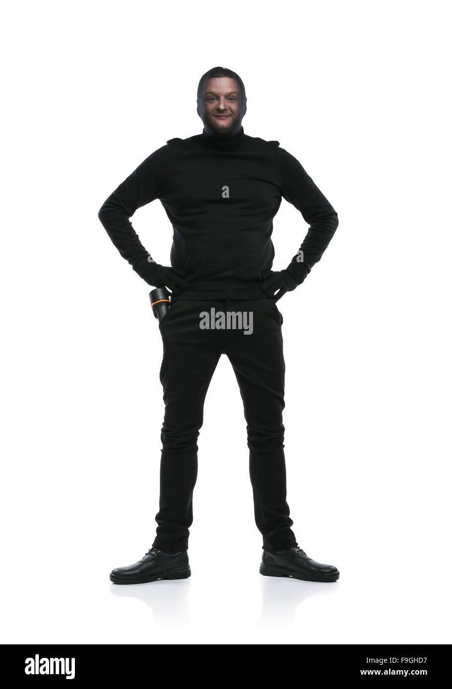 Thief in action with balaclava on his face, dressed in black. Studio shot on white background. Stock Photo