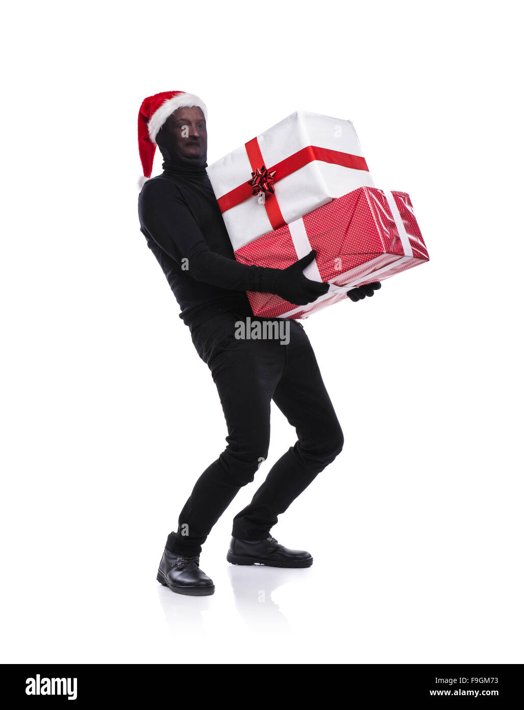 Thief in action carrying presents with balaclava on his face, dressed in black. Studio shot on white background. Stock Photo