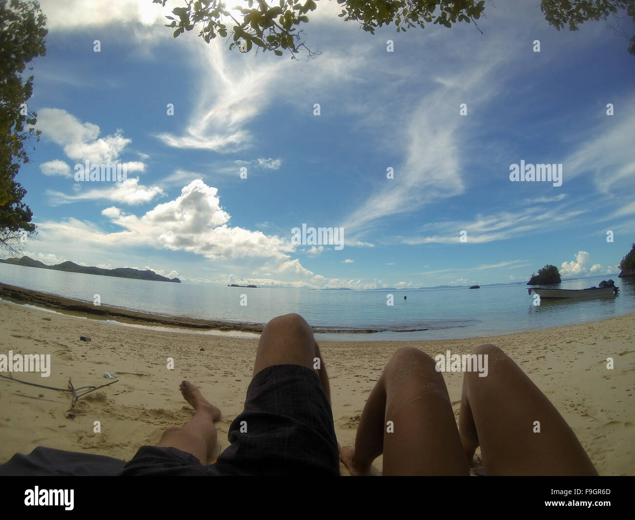 Feet of two person laying on sand beach under blue sky relaxing in Raja Ampat, Papua New Guinea Stock Photo